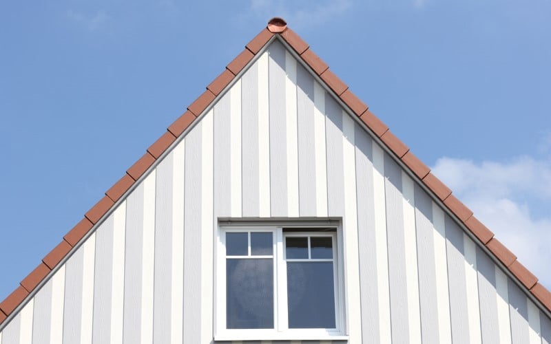 white house siding and orange roof in the middle window above the house blue sky