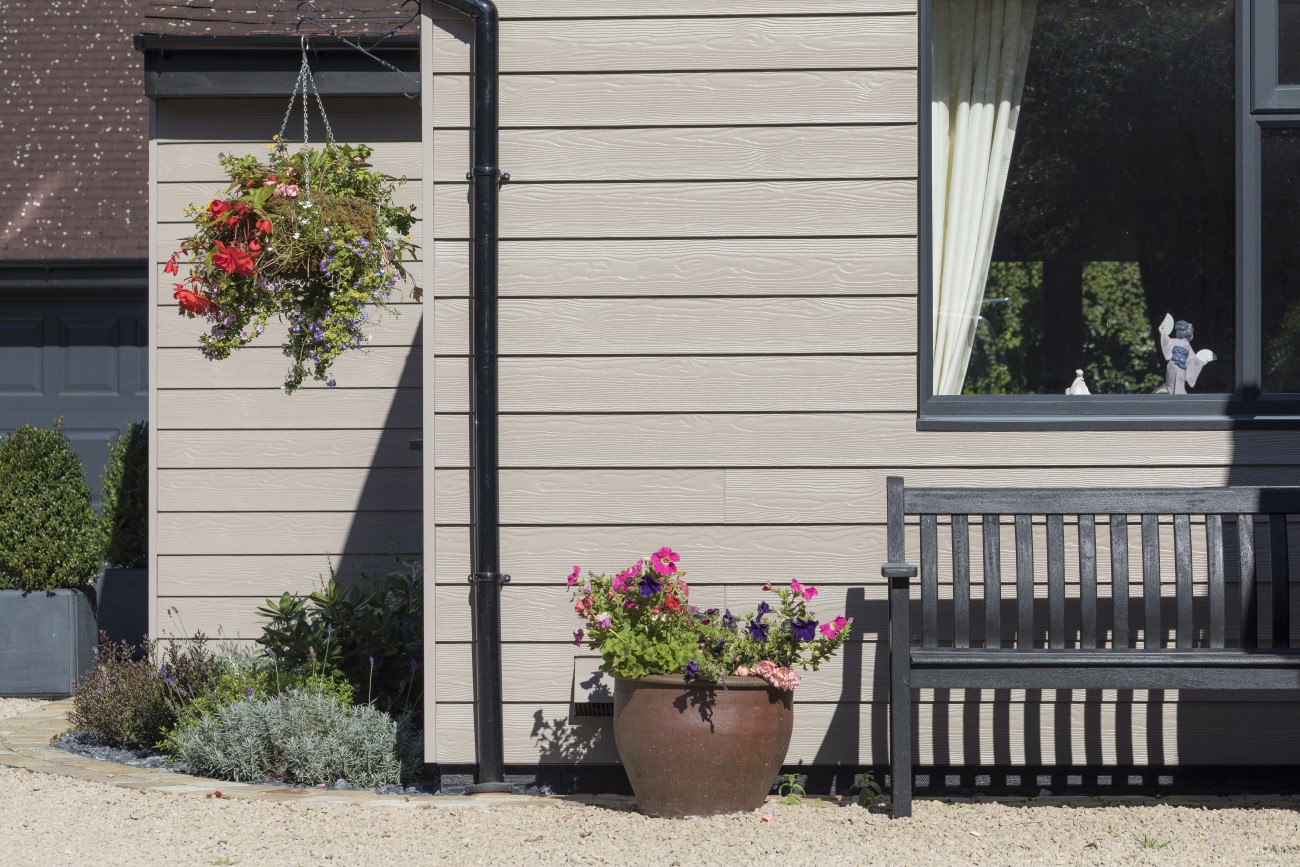 Premium facades of a Cedral home in beige wood texture, adorned with colorful hanging and potted flowers next to a dark wood bench.